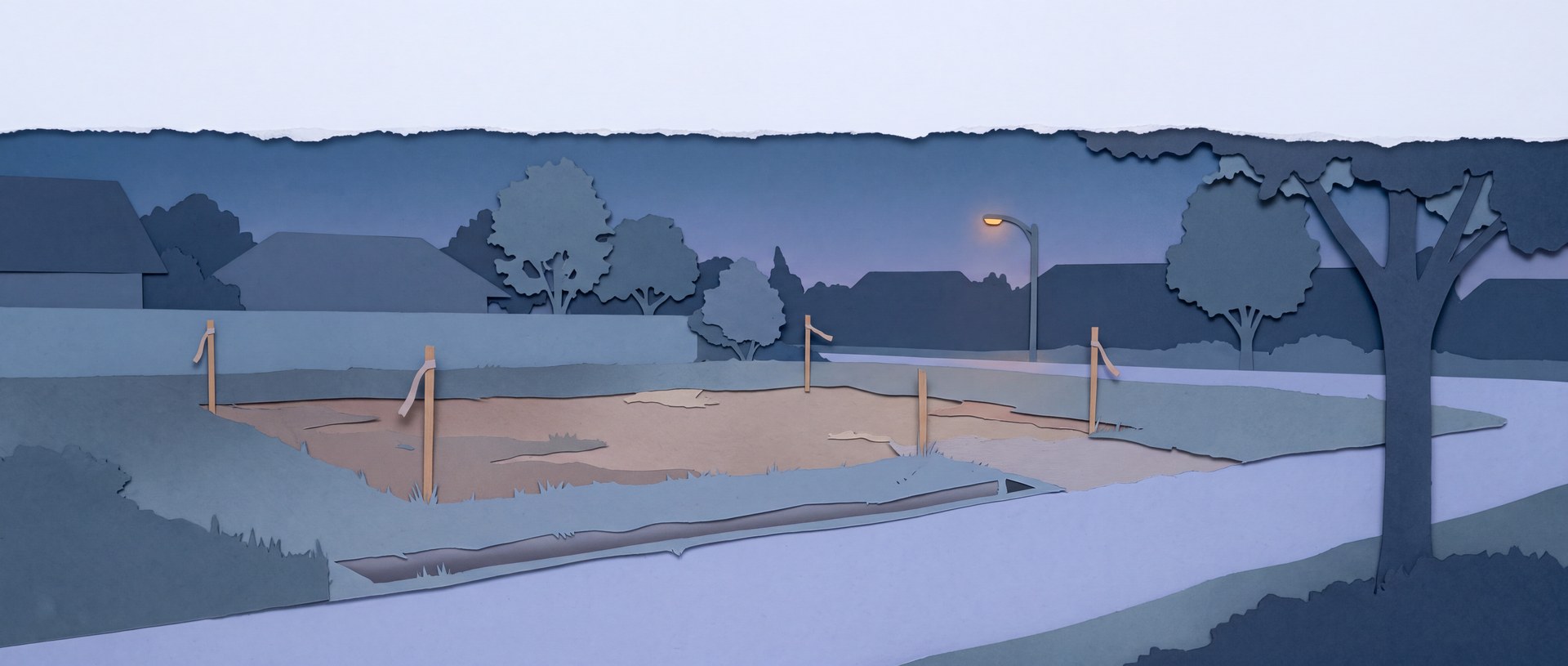 An empty building lot at dusk marked out with survey stakes.