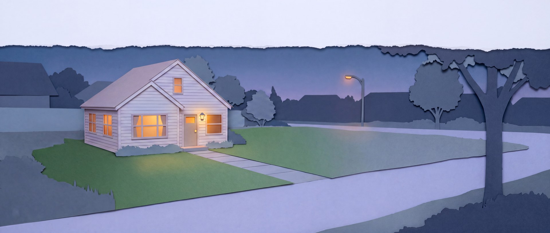 A newly built house at dusk with every window lit, a laid lawn and a paved path.